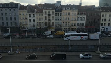 A street view with parked cars, a bus, and buildings with various storefronts.