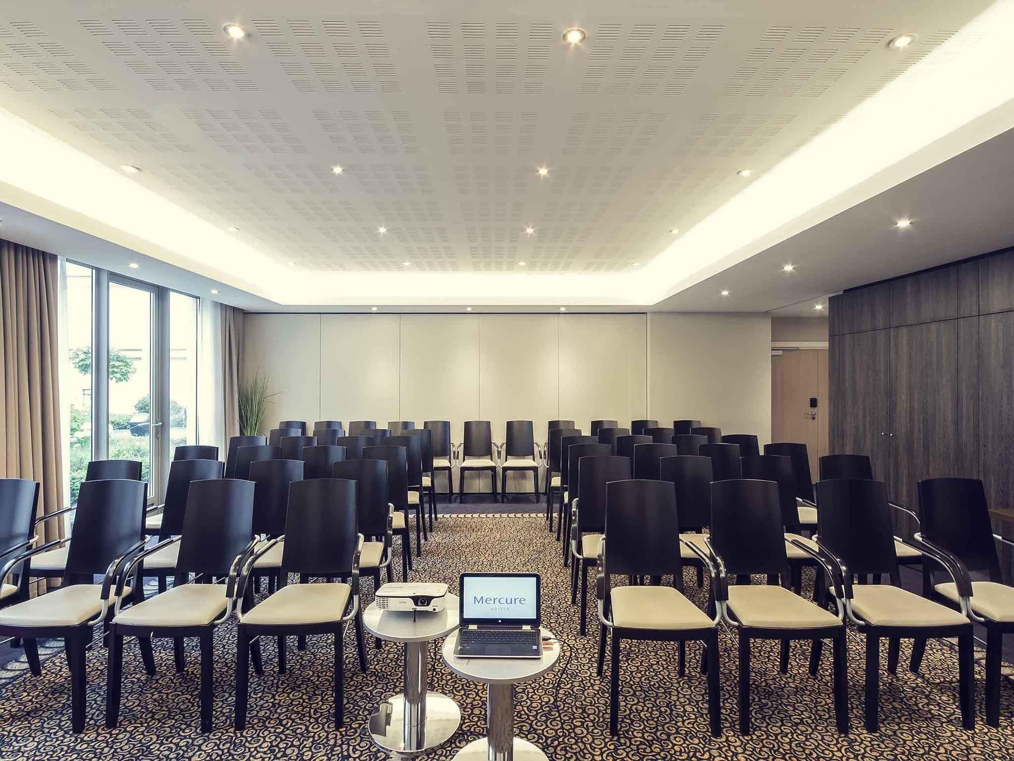 Un salón de conferencias con filas de sillas, una laptop sobre una mesa y un proyector.