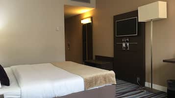 A hotel room with a bed, a television mounted on the wall, a desk, and a trash bin.