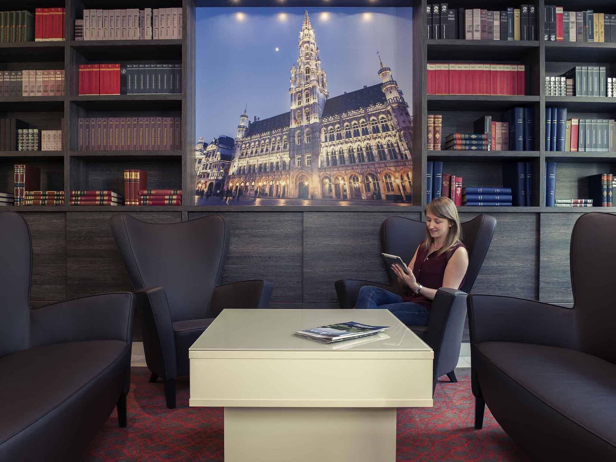 A library with a large framed picture of a historic building, leather armchairs, a small table, and bookshelves filled with books.