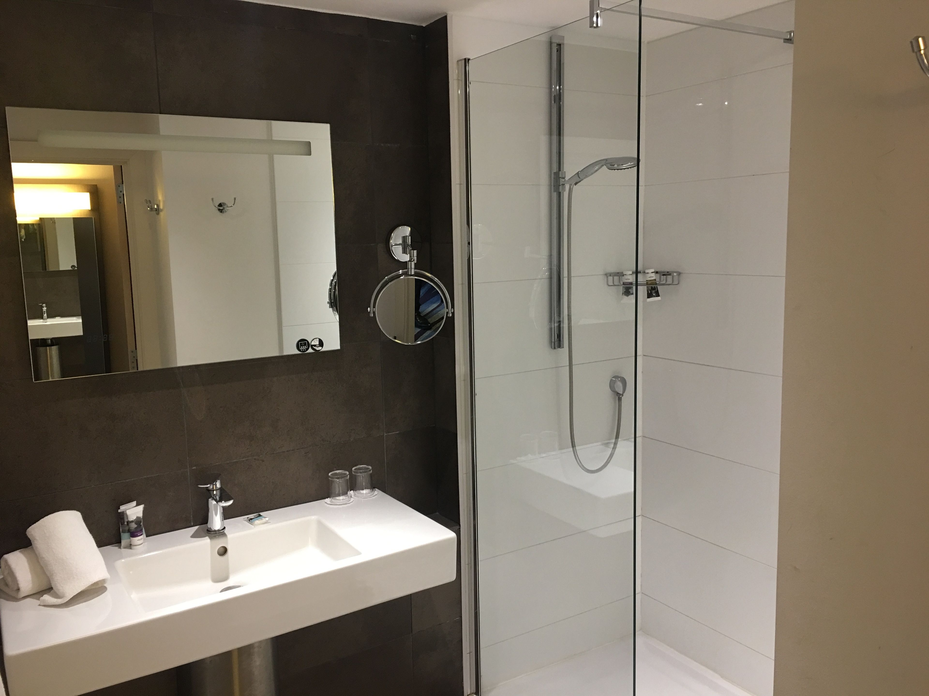 Een moderne badkamer met een witte wastafel, spiegel en douche met glazen wanden.