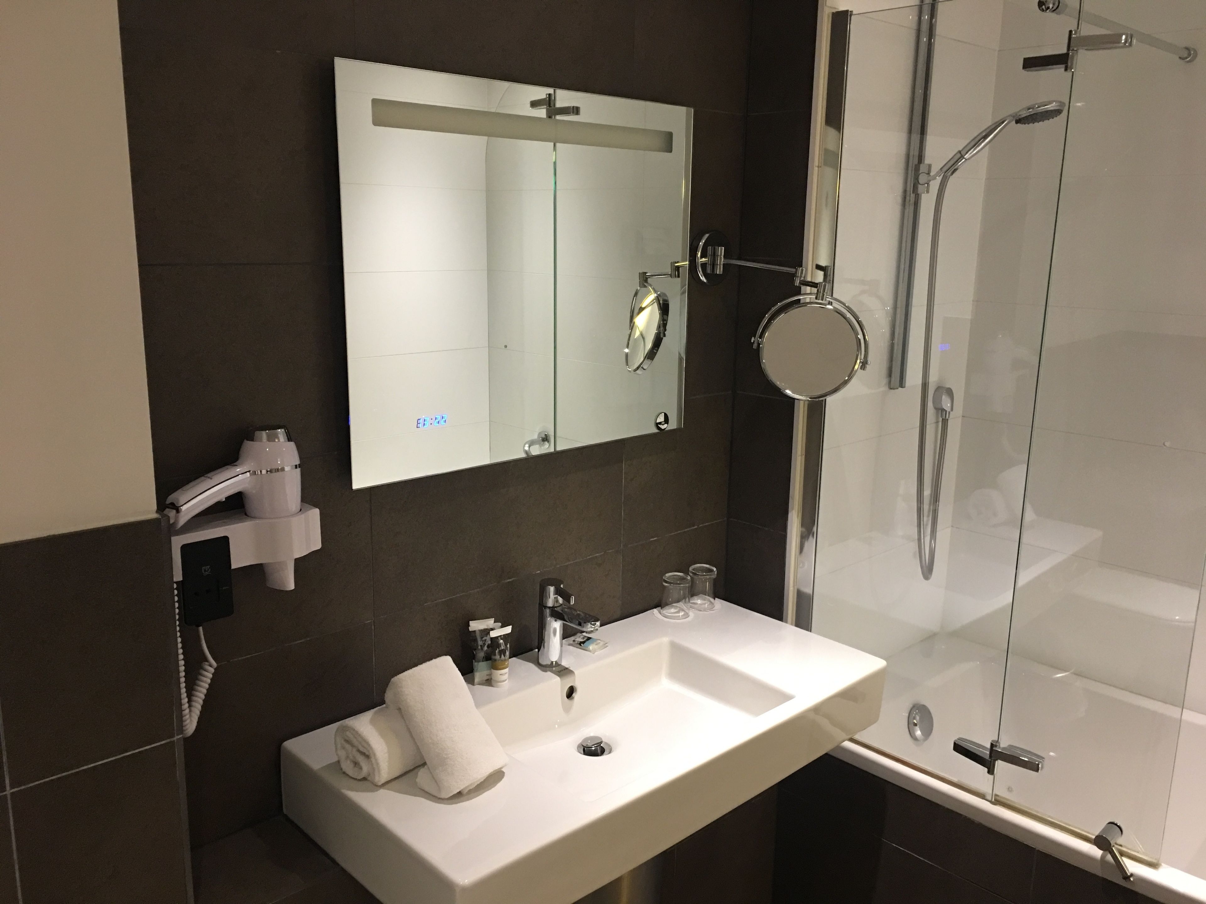 A modern bathroom with a white sink, a mirror, a glass shower enclosure, and a towel rack.