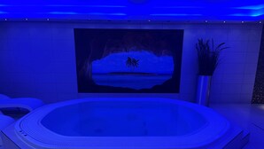 Ein moderner Wellnessraum mit einer großzügigen Whirlwanne, einem Wandbild mit tropischer Szene und einem Topfpflanzen.