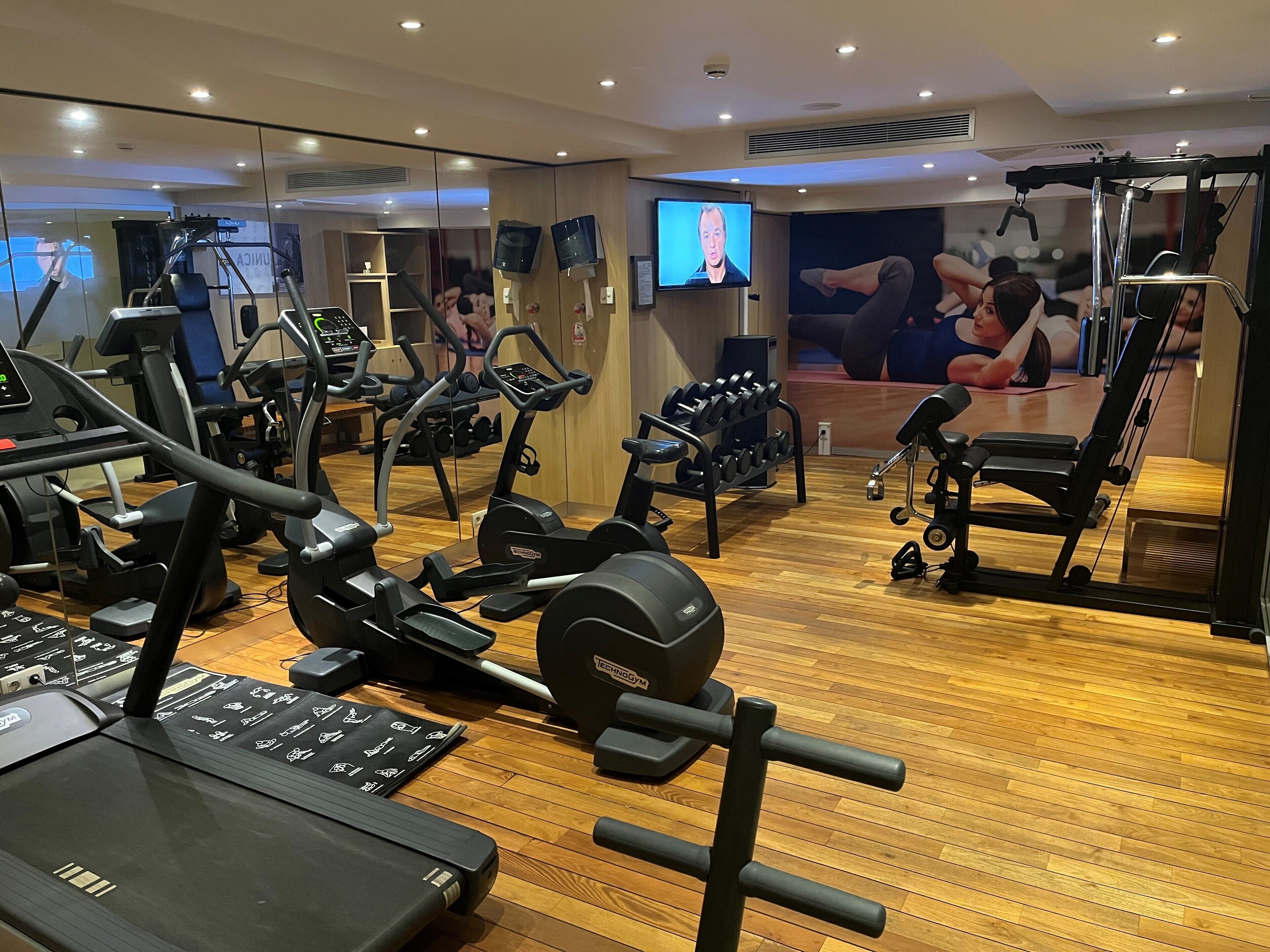 A gym with various exercise equipment, including treadmills, weight machines, and a mirror wall.