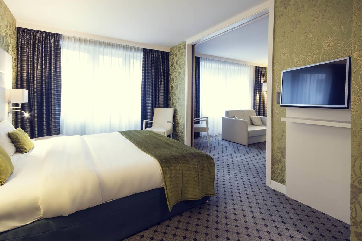 A hotel room with a large bed, a TV mounted on the wall, a sofa, and a chair.