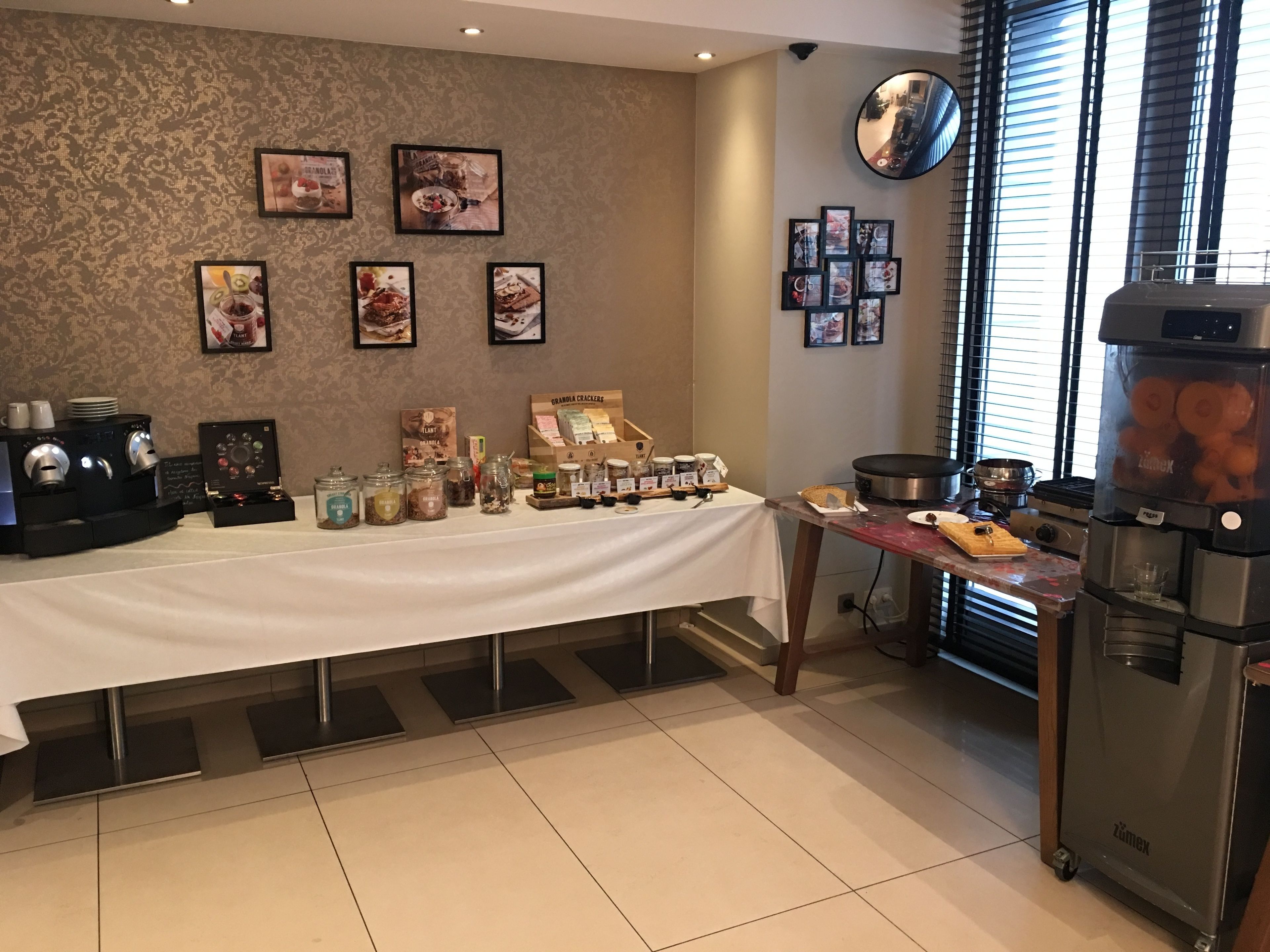 Een keukenhoek met een koffiezetstation, diverse etenswaren en een groot raam met zonwering.