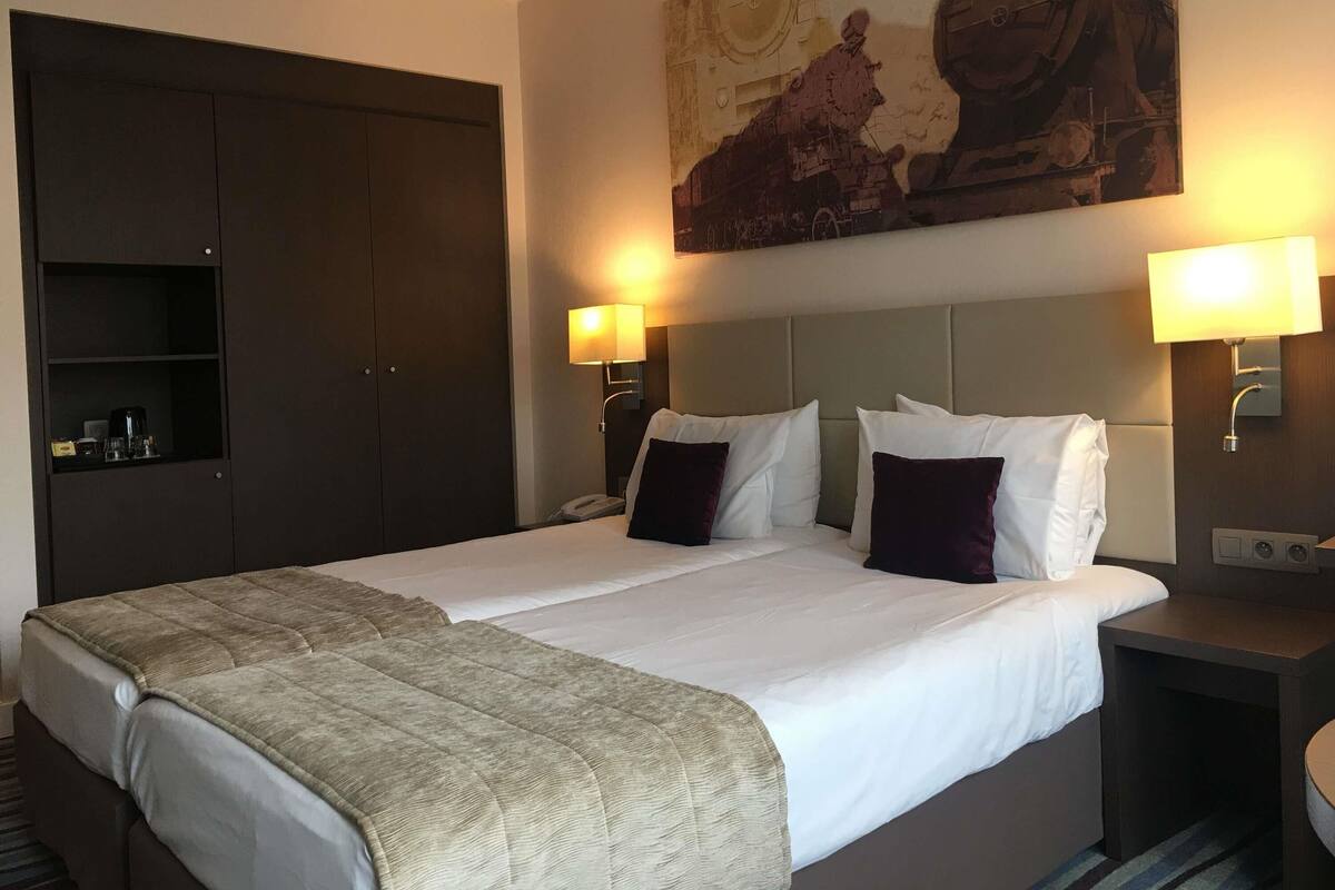 A hotel room with a large bed, two bedside tables, a wardrobe, and a painting on the wall.