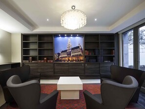 A modern library with a large bookshelf, two black leather chairs, a white coffee table, and a chandelier.