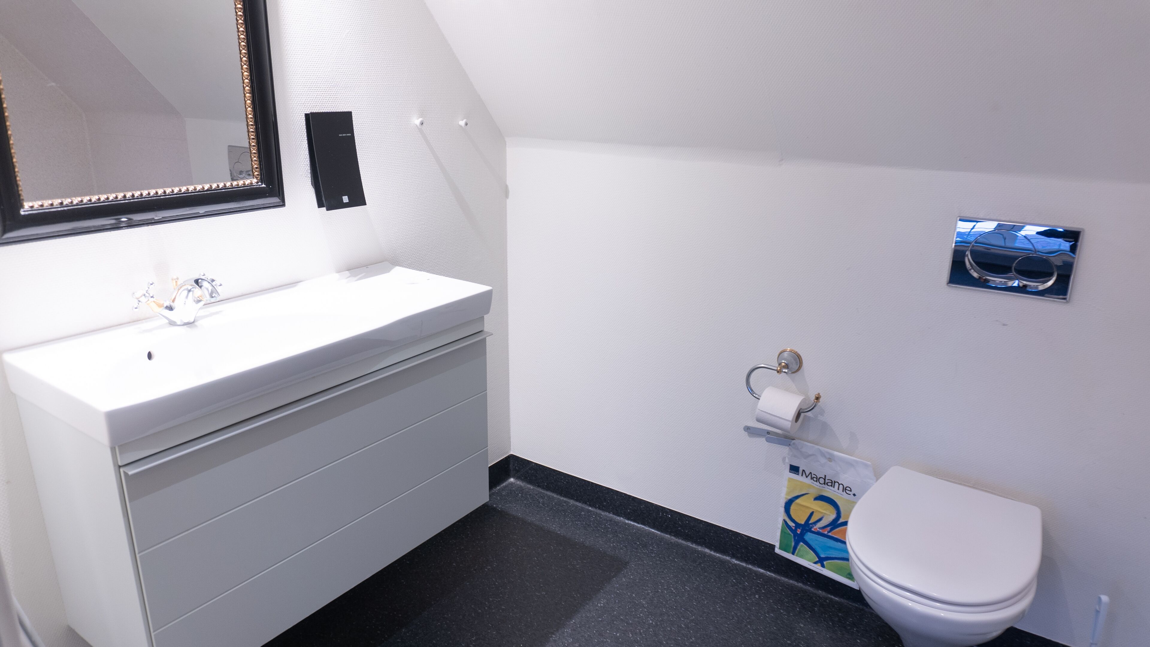Une salle de bain avec un lavabo blanc, un miroir, des toilettes et une petite poubelle.
