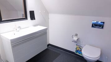 A bathroom with a white sink, mirror, toilet, and a small trash bin.