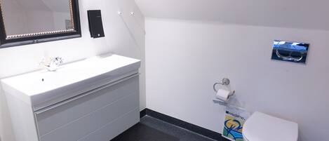 A bathroom with a white sink, mirror, toilet, and a small trash bin.
