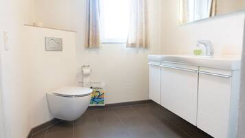 Et lille, rent badeværelse med toilet, vask og et vindue med gardiner.