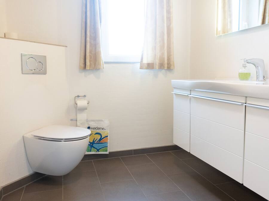 Une petite salle de bain propre, équipée de toilettes, d’un lavabo et d’une fenêtre avec des rideaux.
