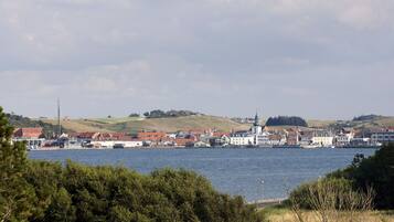 Un pueblo costero con edificios a lo largo de la orilla, una imponente aguja de iglesia y una colina al fondo.