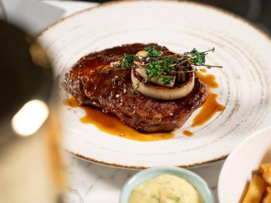 A steak with a sauce and garnish on a plate, accompanied by fries and a small bowl of sauce.