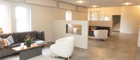 Un interior espacioso y moderno con un sofá gris, un sillón blanco y una mesa de centro de madera. Hay una planta pequeña sobre la mesa y un cuadro en la pared.