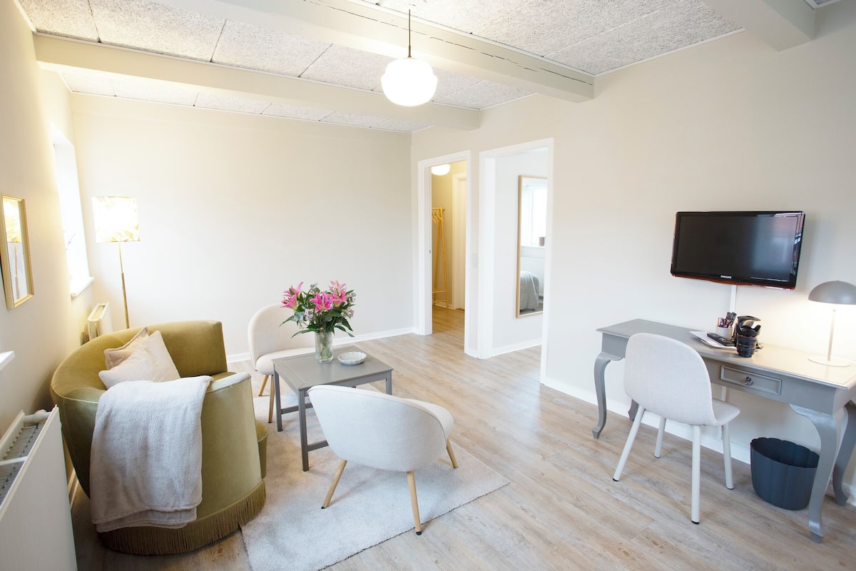 A modern living room with a sofa, chairs, a desk, a TV, and a vase with flowers.
