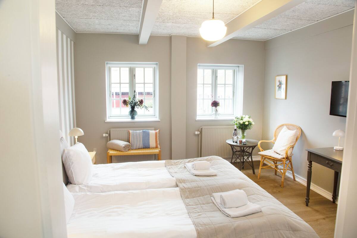 A hotel room with two beds, a chair, a table, and a TV.