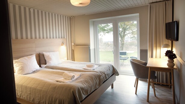 A hotel room with two beds, a desk, a chair, a television, and a view of the outdoors. - HotelVFjorden (Lemvig)