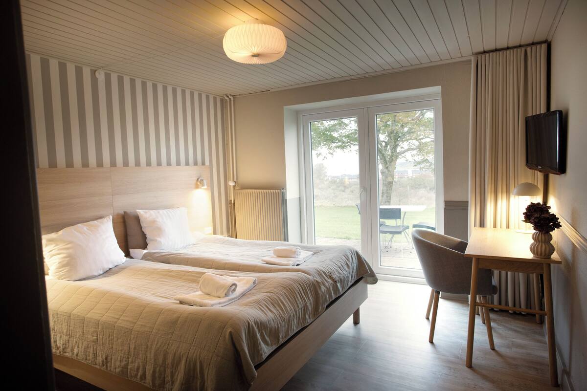 A hotel room with two beds, a desk, a chair, a television, and a view of the outdoors.