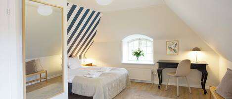 A bedroom with a bed, a desk, a chair, a mirror, a window, and a radiator.