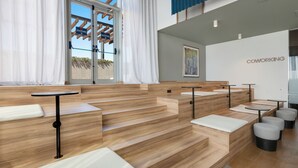 Ein moderner Coworking-Space mit Holzböden, weißen Sitzgelegenheiten mit Polsterung und einer Glastür zum Außenbereich.