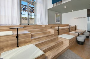 Um espaço de coworking moderno com piso de madeira, assentos acolchoados brancos e uma porta de vidro que dá para o exterior.