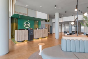 Recepção de hotel com parede verde, balcão de atendimento e área de estar.