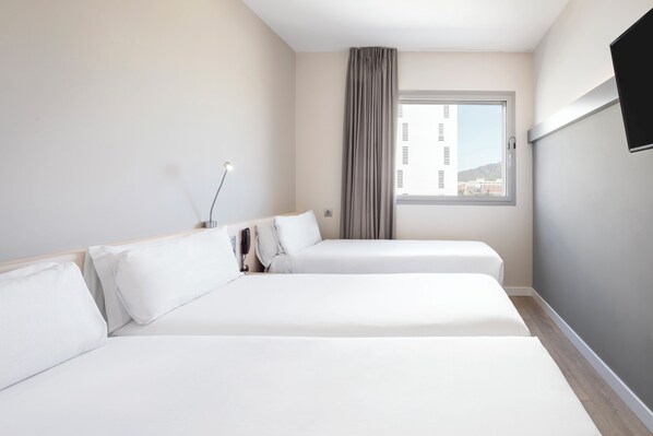 Habitación de hotel con dos camas, ventana con vistas, televisor de pantalla plana y mesita de noche con lámpara.