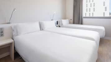 Habitación de hotel con dos camas individuales, una mesita de noche, una lámpara y una ventana con persianas.