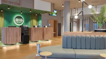 Zona de recepción de un hotel moderno con una pared verde, un mostrador de recepción, un área de estar y una pantalla de televisión.
