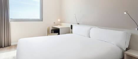 A modern hotel room with a large bed, a desk, and a chair.