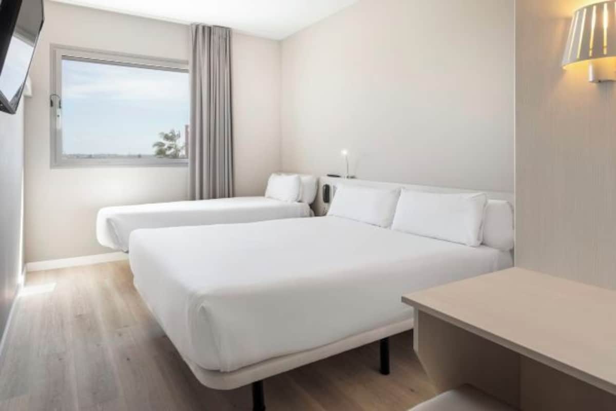 Ein Hotelzimmer mit zwei Betten, einem Fernseher, einem Nachttisch, einer Lampe und einem Fenster mit Blick.