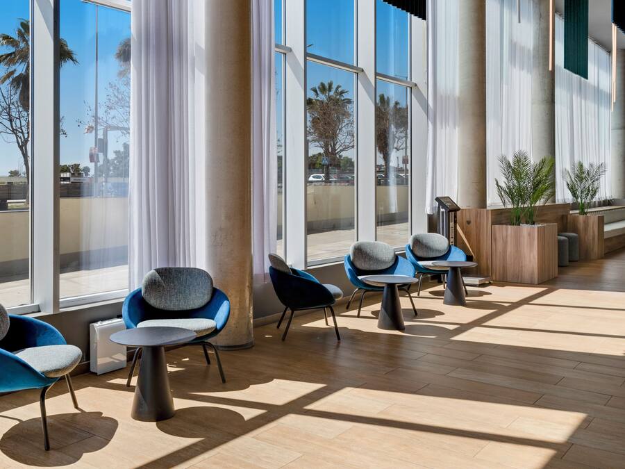 Un espacio interior moderno con ventanas amplias, sillas azules y grises, y suelo de madera.
