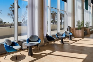 Espaço interno moderno com janelas amplas, cadeiras azuis e cinzentas, e piso de madeira.
