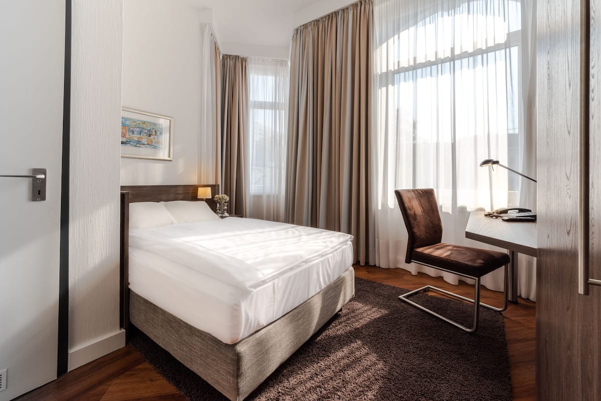 Habitación de hotel con cama, escritorio, silla y ventana con cortinas.