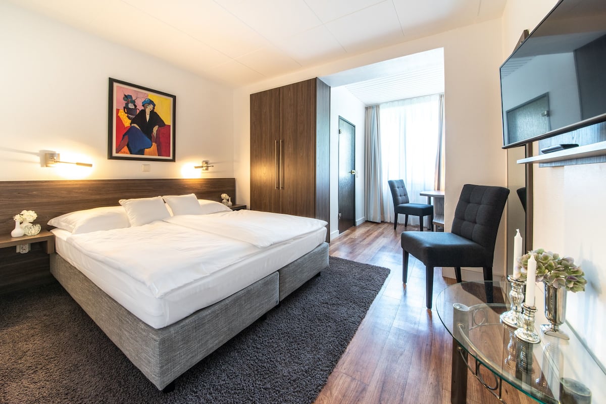 Una habitación de hotel moderna con una cama grande, una mesa de centro de vidrio, un televisor y un cuadro en la pared.