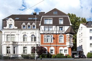 Una hilera de edificios residenciales de tres pisos con estilos arquitectónicos variados, incluyendo un edificio en esquina con balcón y uno con entrada de garage visible.