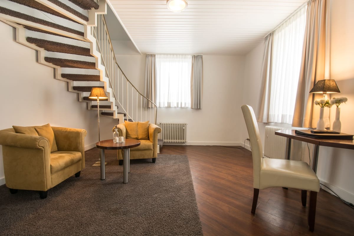 Una sala de estar con una escalera, dos sofás, una mesa de centro y una lámpara.