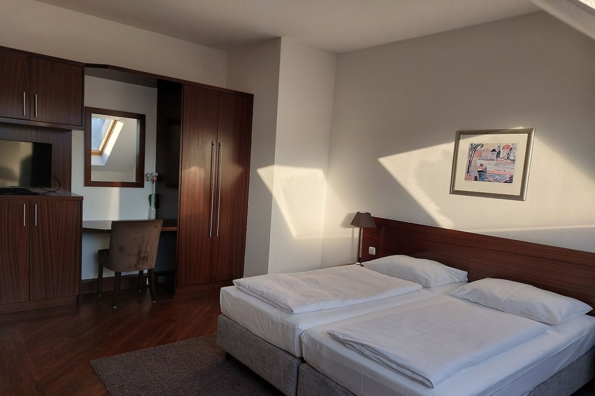 Habitación de hotel con cama doble, escritorio con silla, armario y un cuadro enmarcado en la pared.