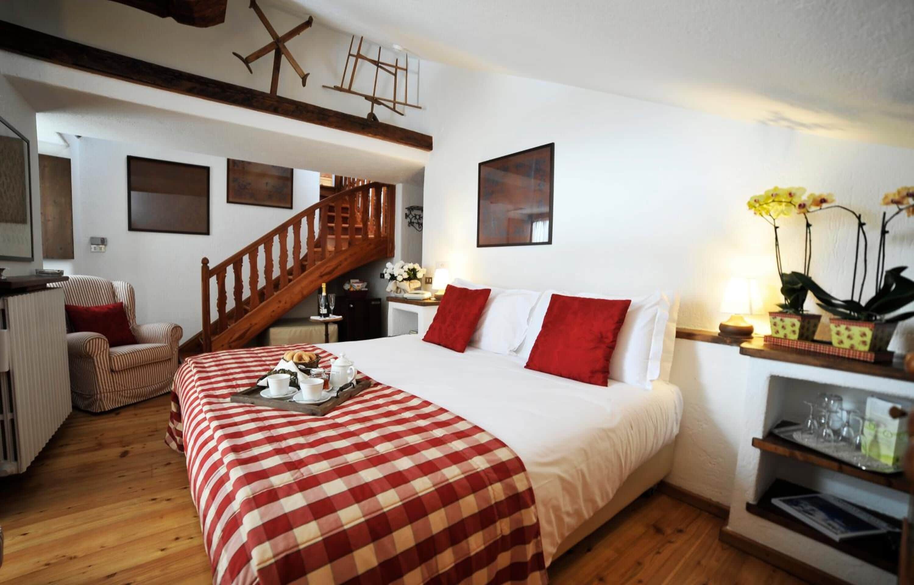 Un dormitorio acogedor con una escalera de madera, una cama con ropa de cama roja y blanca, una silla y una mesita con una bandeja de desayuno.