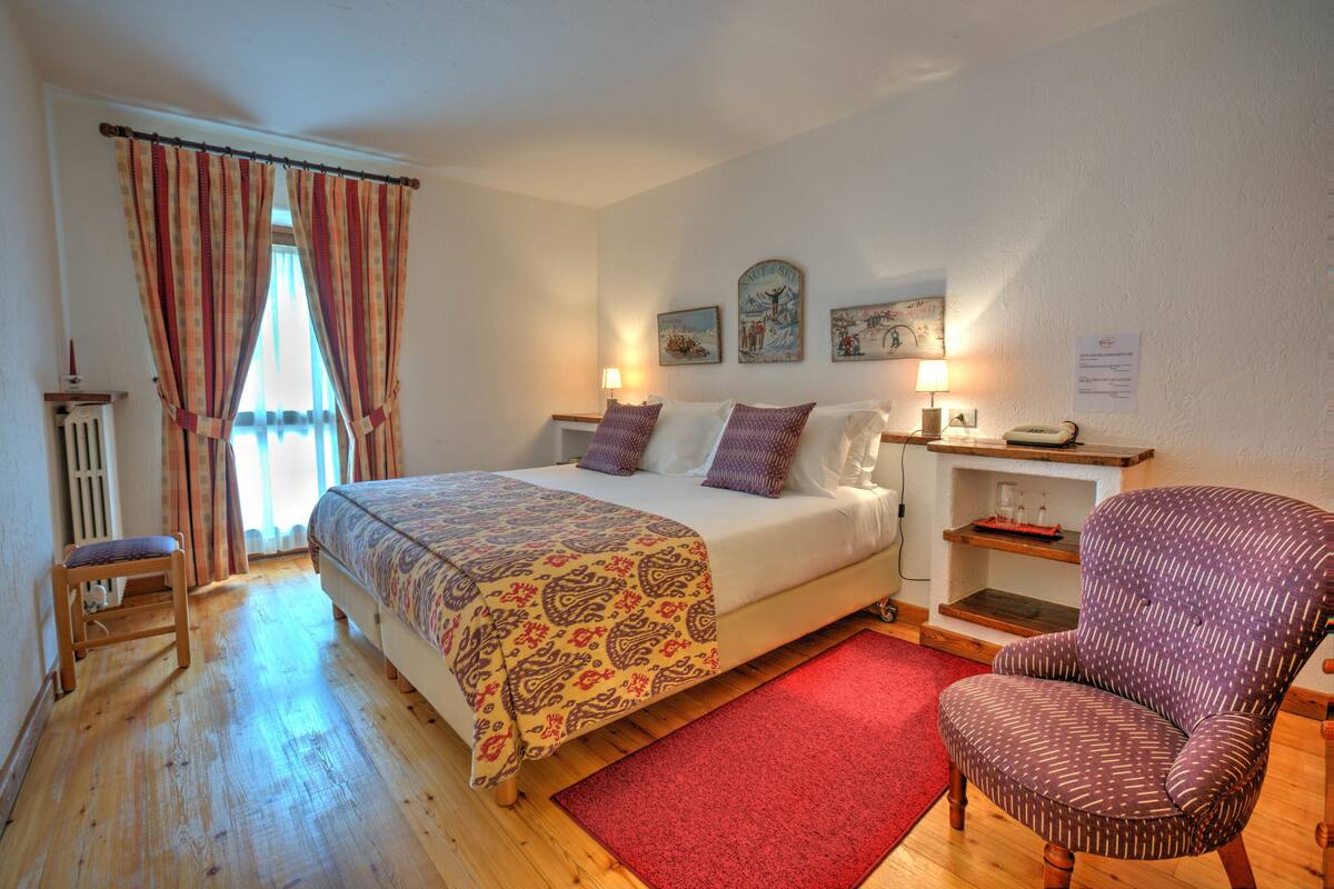A bedroom with a bed, a chair, a red rug, and a wooden floor.