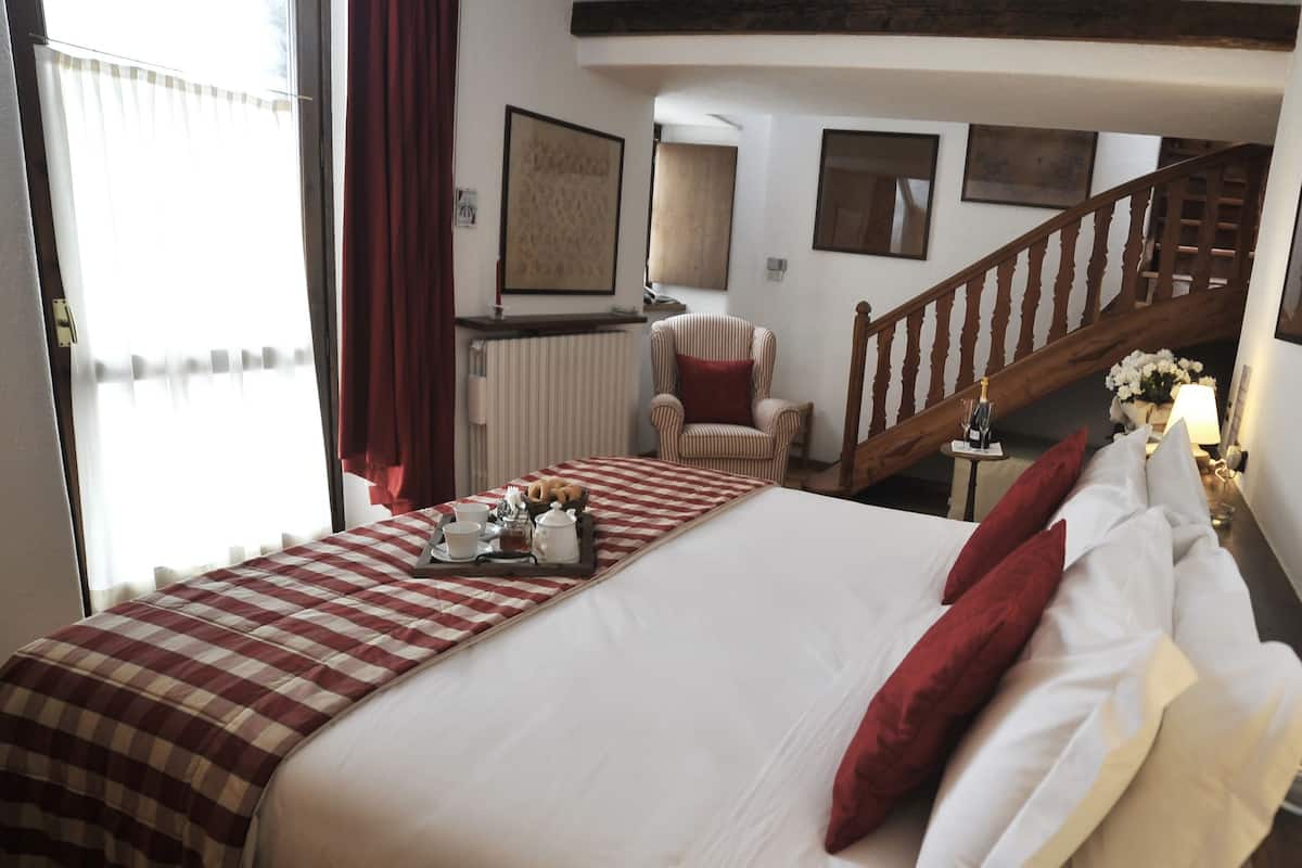 A hotel room with a large bed, a chair, a wooden staircase, and a view of the outside.