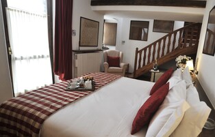 Habitación de hotel con una cama grande, una silla, una escalera de madera y vistas al exterior.