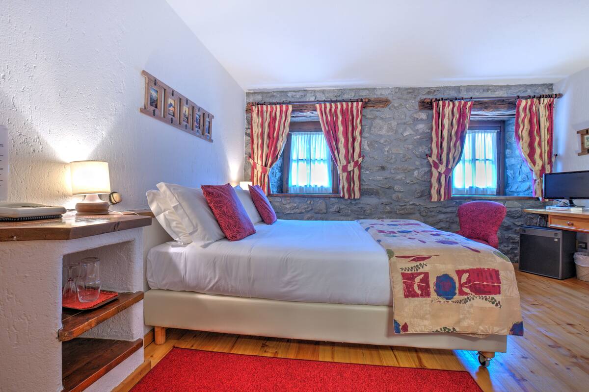 A bedroom with a bed, a desk, a chair, and a stone wall.