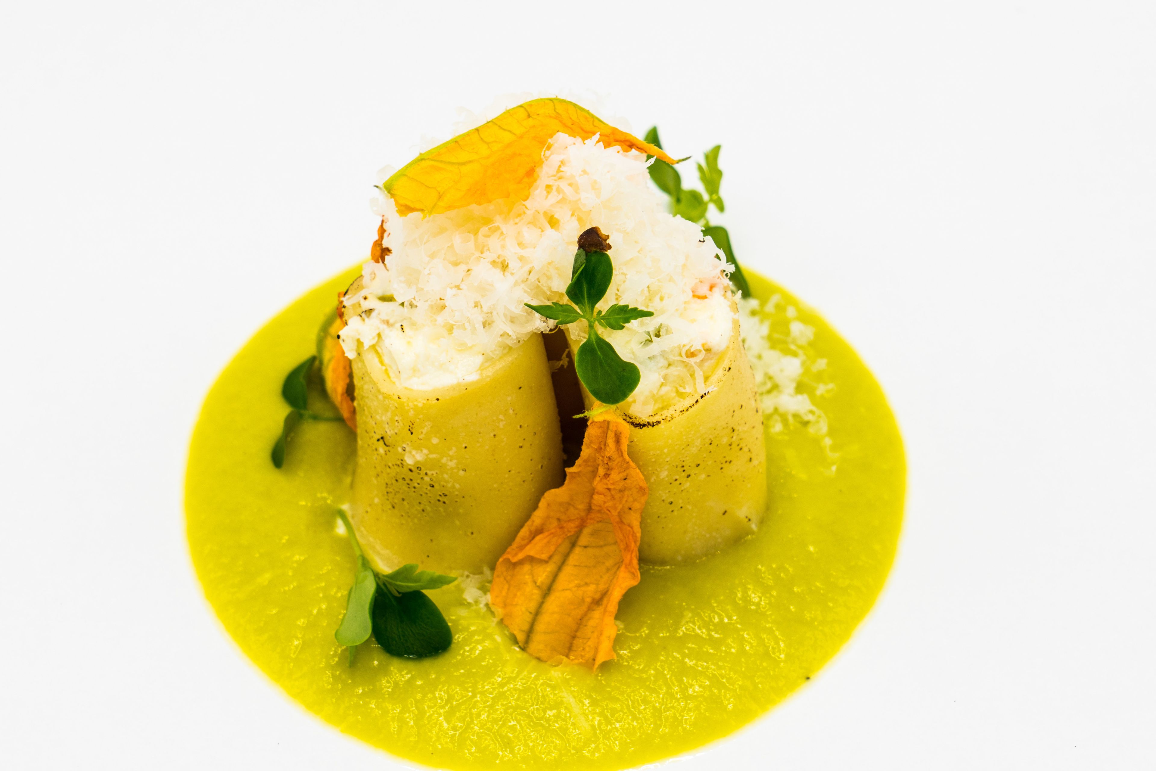 A dish with a yellow sauce, garnished with green leaves and a crispy element.
