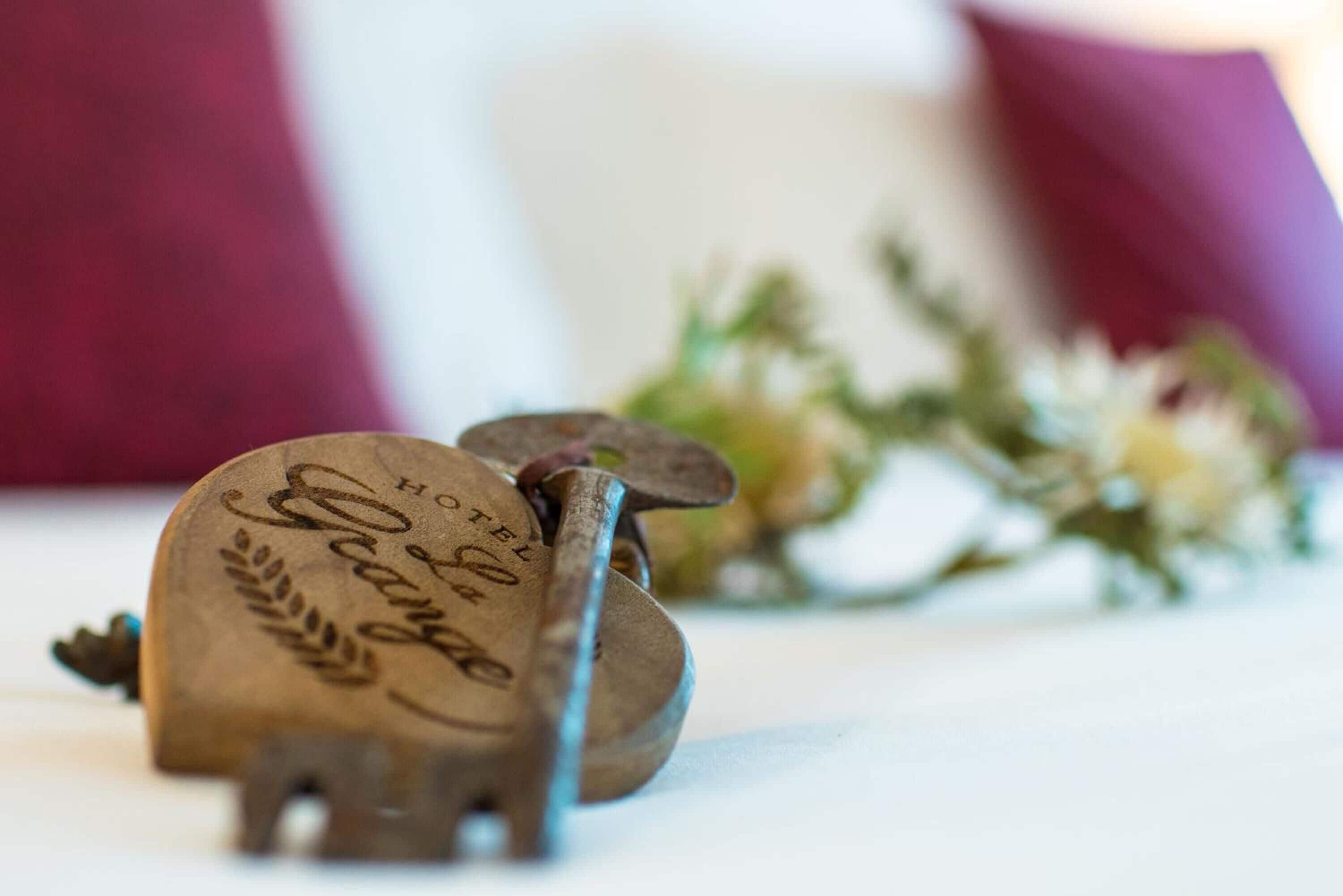A vintage key with the inscription "Hotel George" on a white surface, accompanied by a blurred floral arrangement.