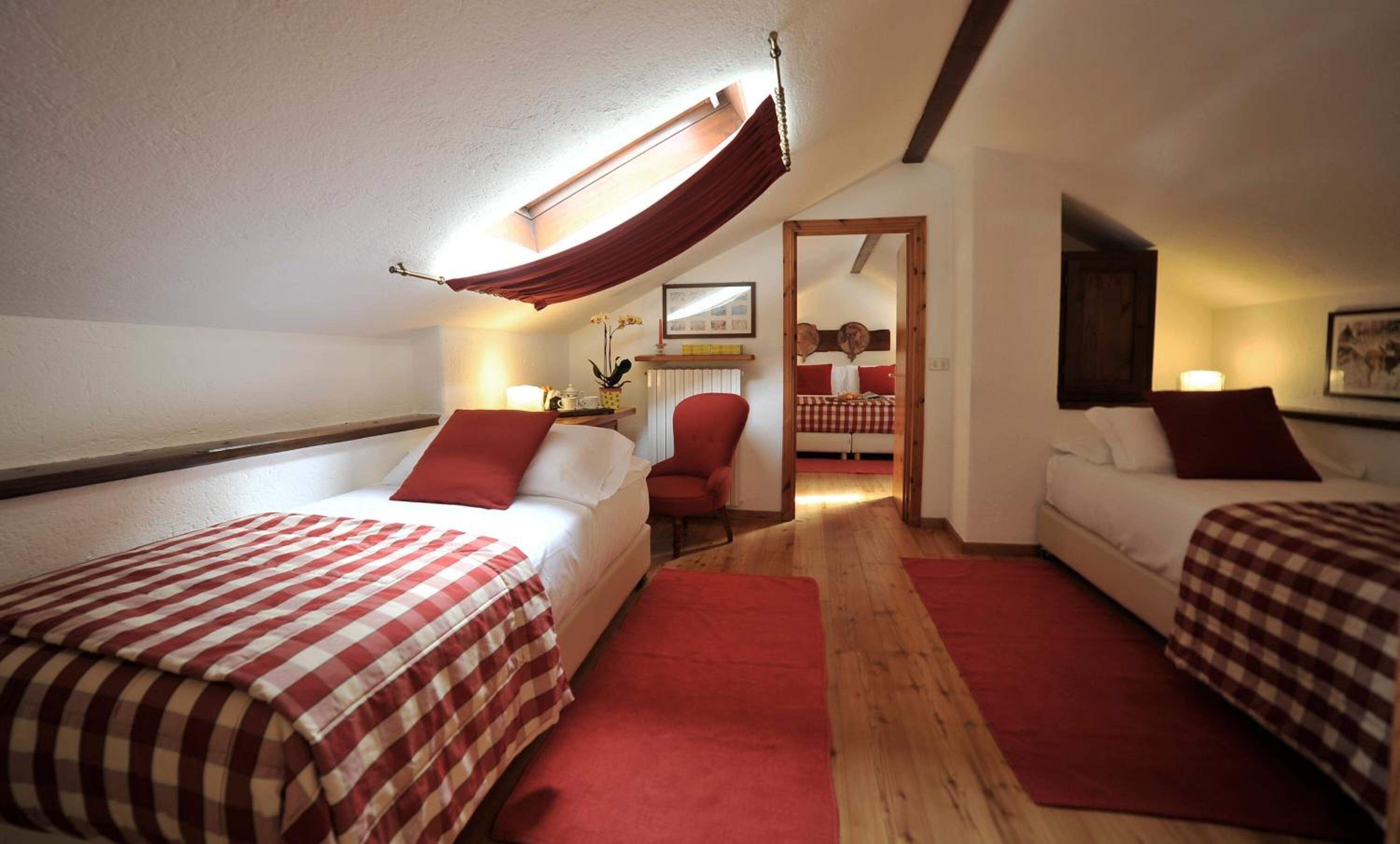 Quarto com duas camas, uma cadeira vermelha e piso de madeira.