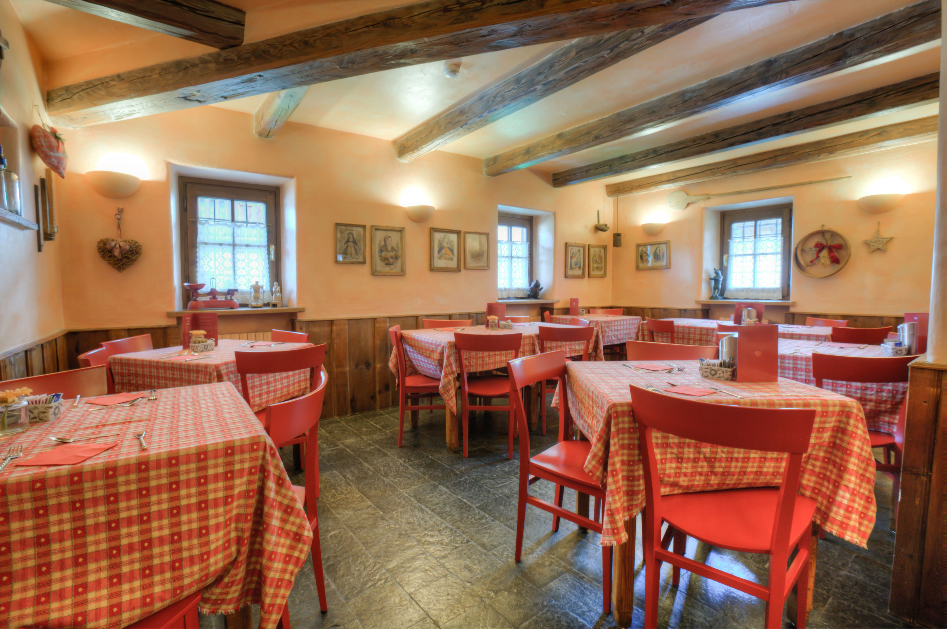 A dining area with multiple tables and chairs, wooden beams on the ceiling, and framed pictures on the walls.