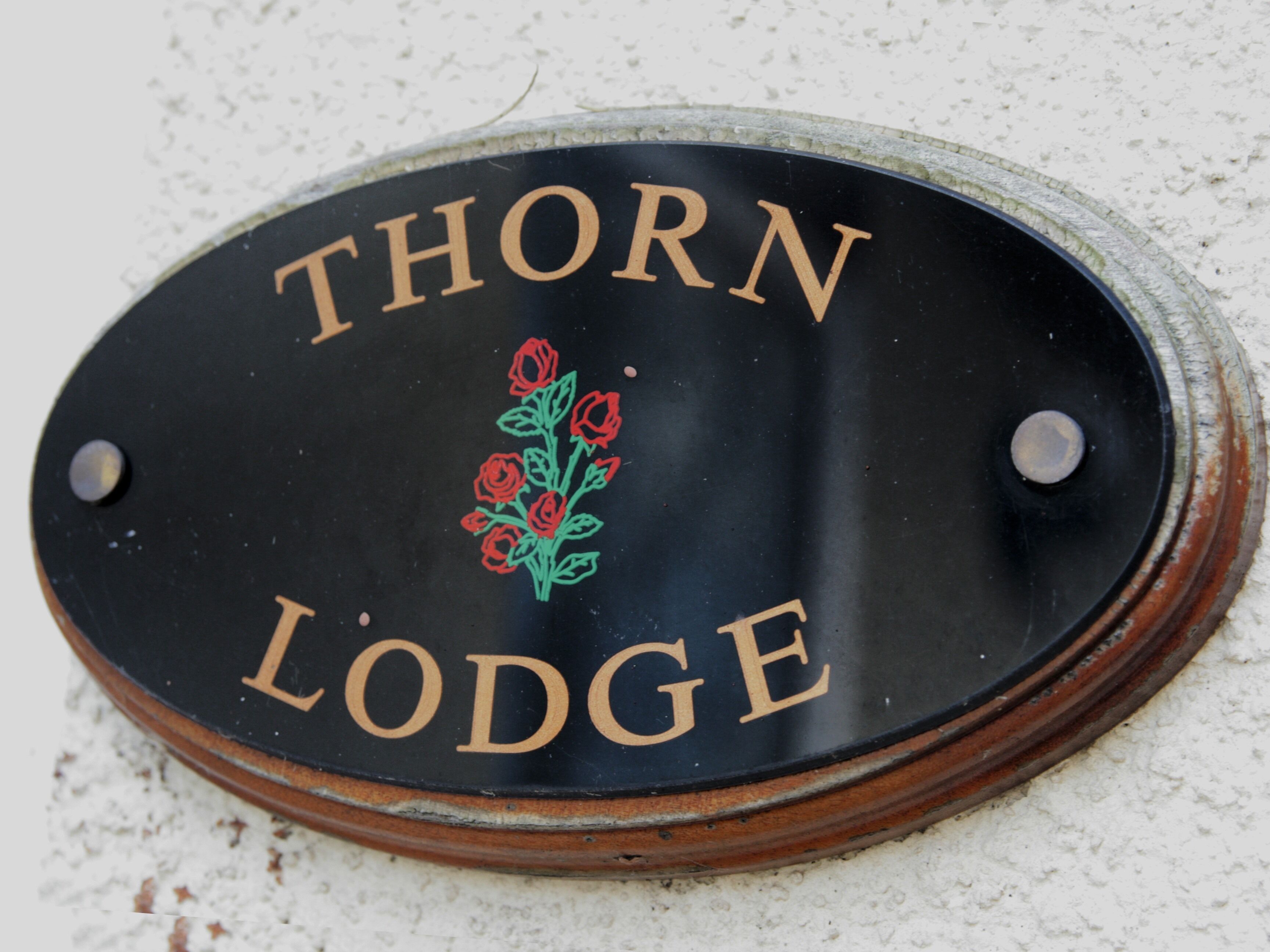 A black sign with gold lettering that reads "THORN LODGE" and a red rose design.